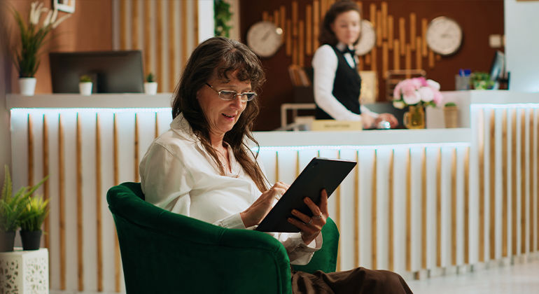 Hotel check-in scene showing a guest using a tablet in a stylish lobby with a receptionist at the front desk and elegant decor elements.