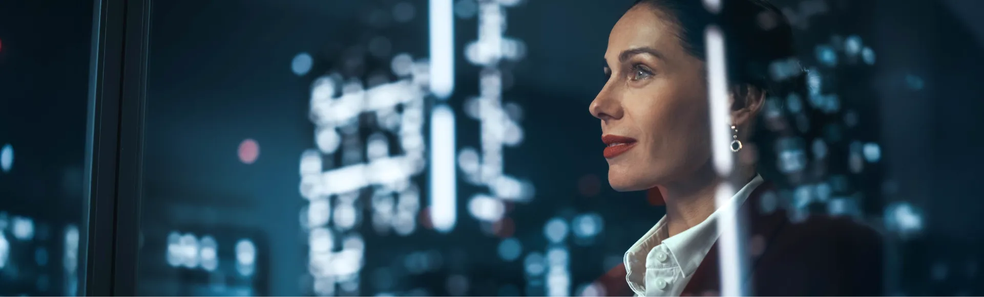 Thoughtful businesswoman observing a brightly lit city skyline at night.