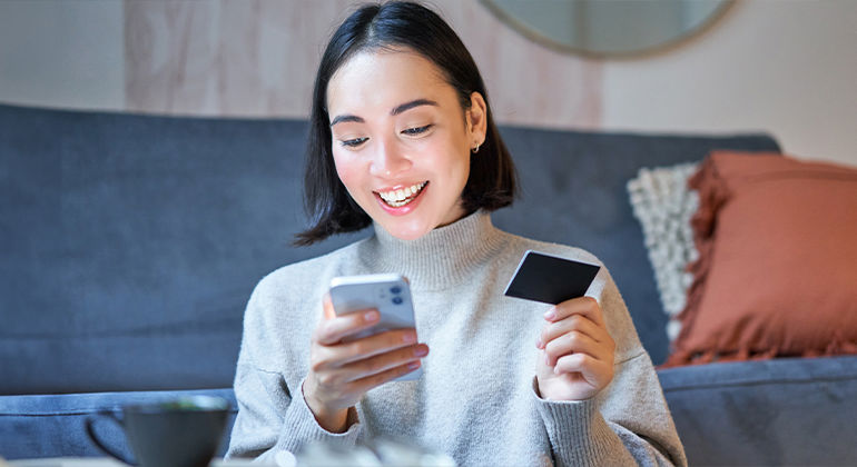 Person sitting on a couch holding a smartphone and a credit card, making an online payment.