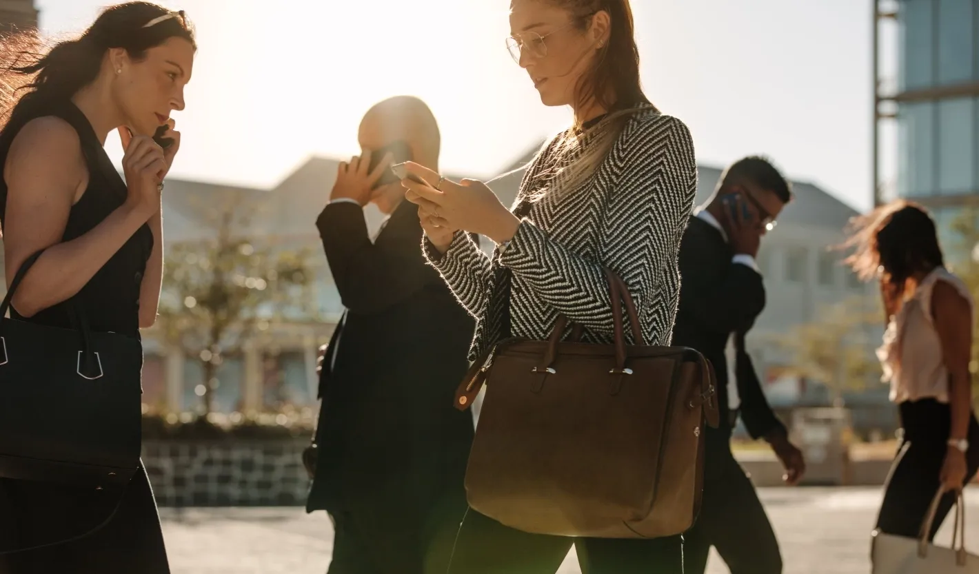Professionals walking outdoors while using smartphones, representing digital connectivity in daily work life.