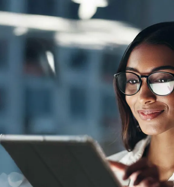 Woman wearing glasses smiling while working on a digital device.