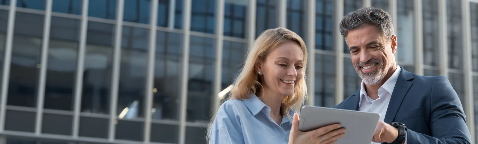 Two business professionals reviewing information on a tablet outside an office building.