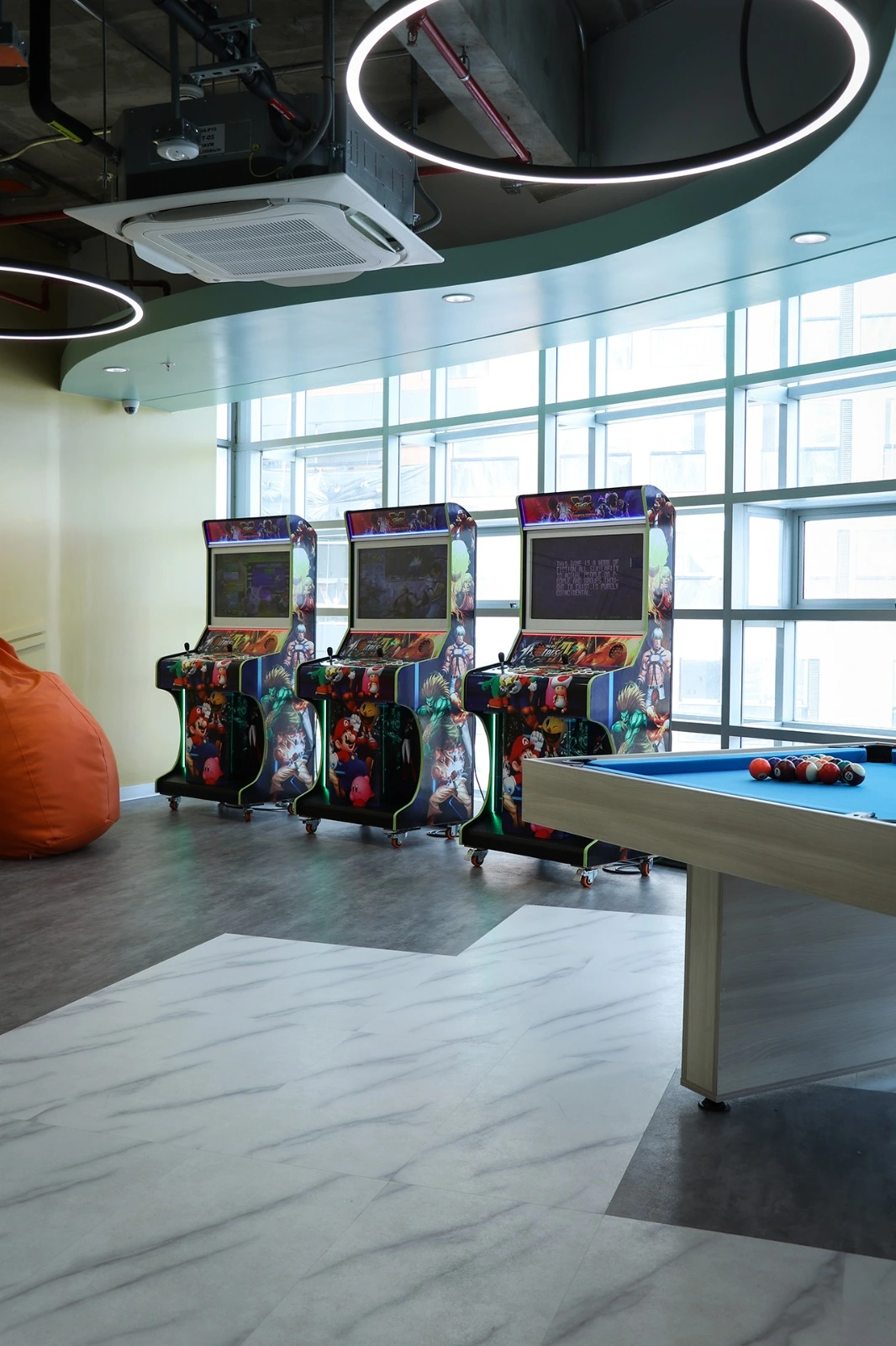 Game room with arcade machines and a pool table in a modern office space.